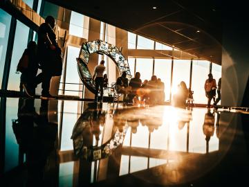 A bright room with a large sunlight window and people walking around