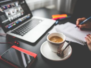Image of an open laptop on a desk with a hand and cup of coffee