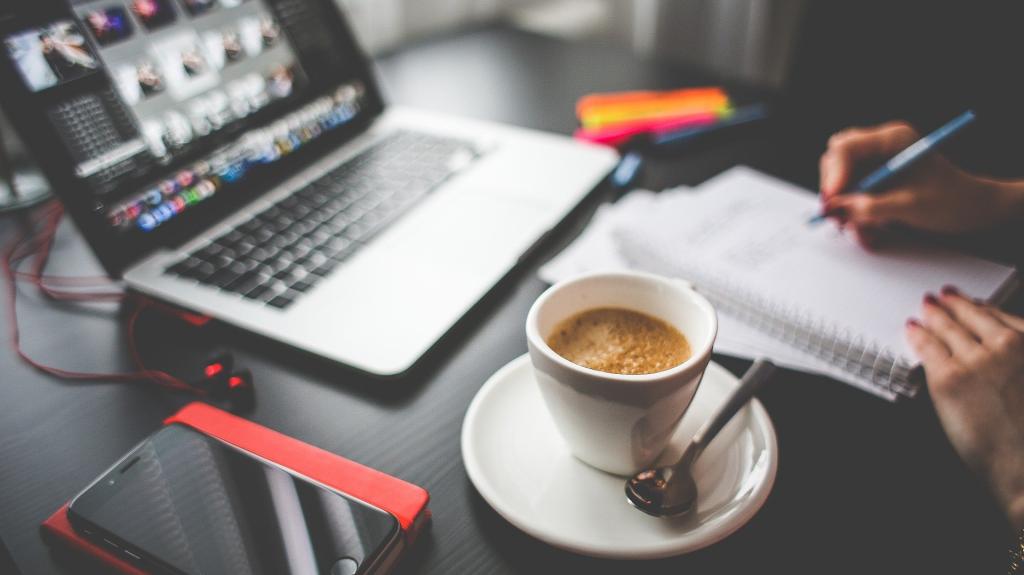 Image of an open laptop on a desk, a hand and a cup of coffee